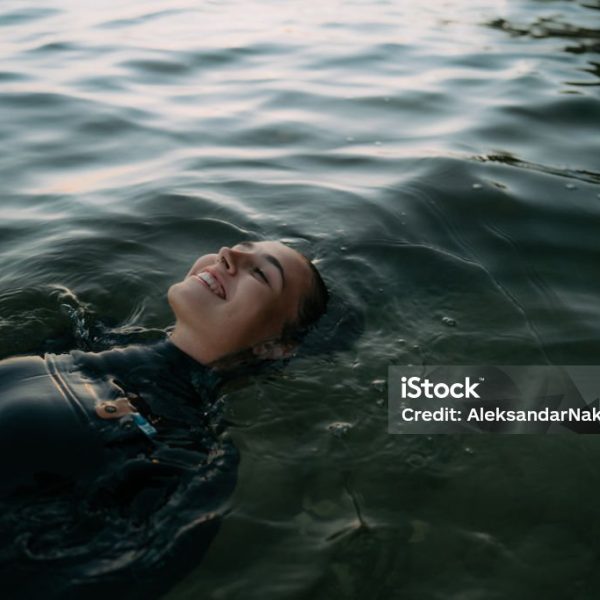 Photo of a young woman relaxing in the cool ocean water. She is wearing a wetsuit.